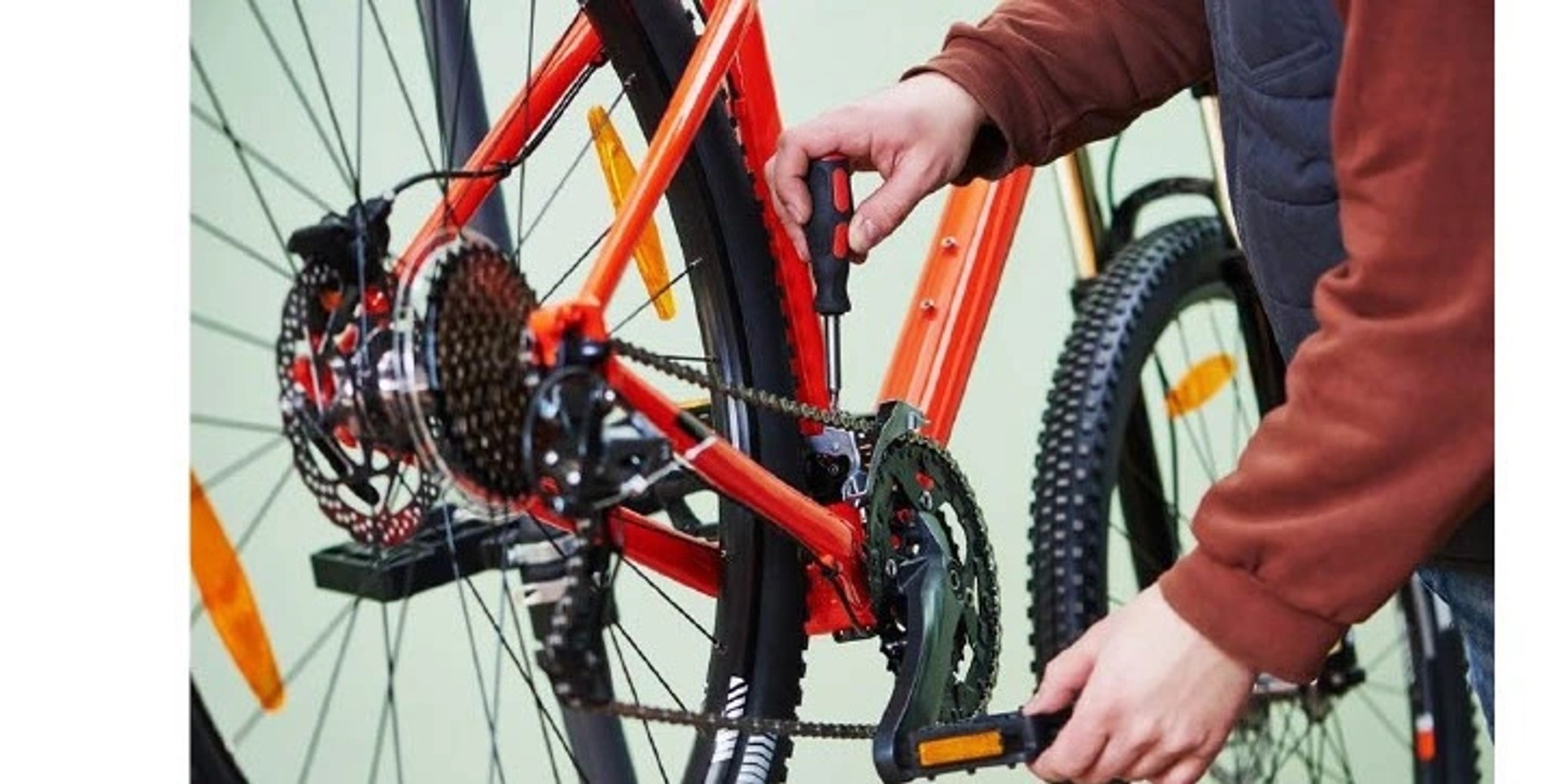 A person with a screwdriver performing maintenance on a bicycle drive train.